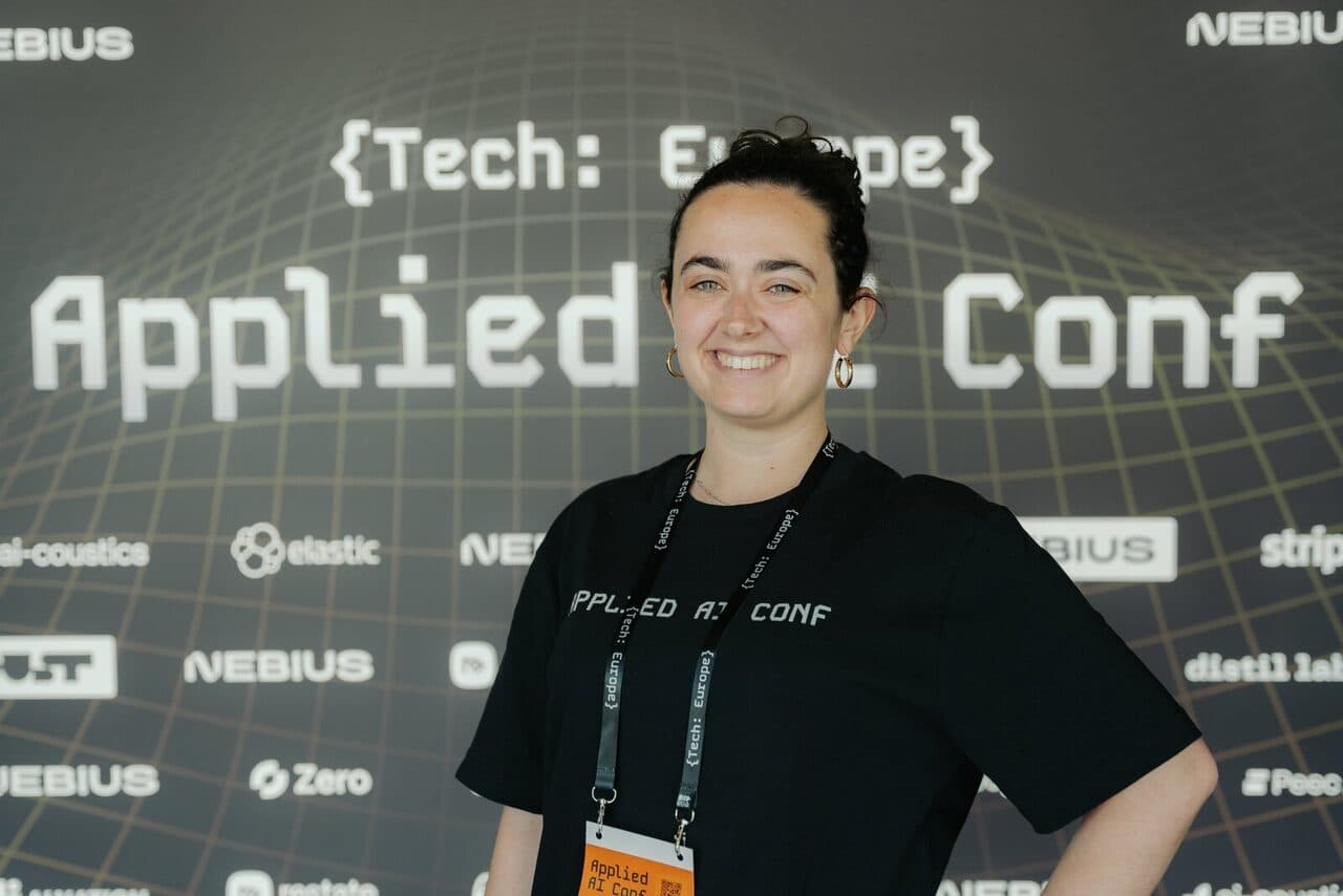 A volunteer in front of the Applied AI Conf 2026 logo wall
